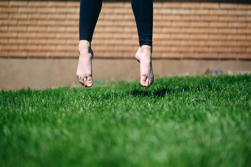 A pair of feet jumping off a lush, green lawn. Photo by Sharon McCutcheon.